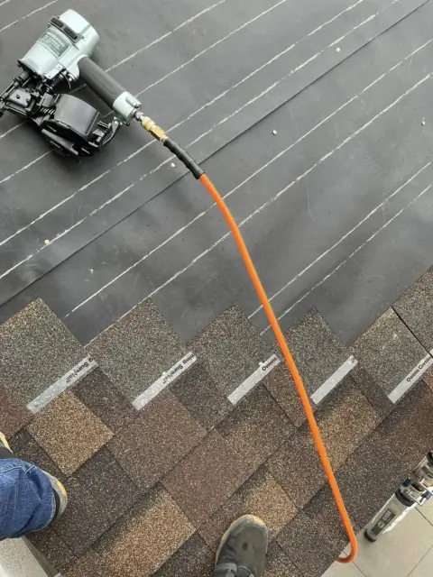 Nail gun on a roof as new architectural shingles go on over underlayment