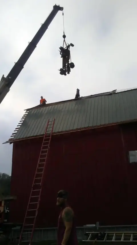 Crane lifting a worker and materials onto a barn roof
